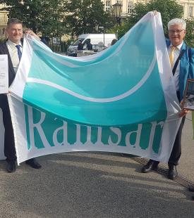 Vier Personen halten ein Banner mit der Aufschrift 'Ramsar' zwischen sich