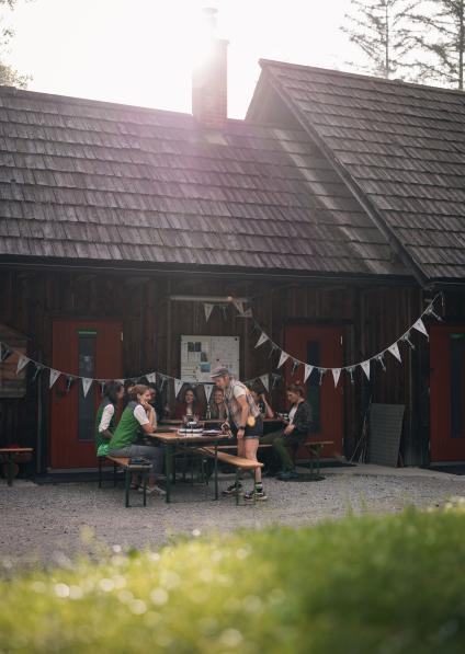 Vor einem Haus sitzt eine Gruppe von Menschen an Bierbänken